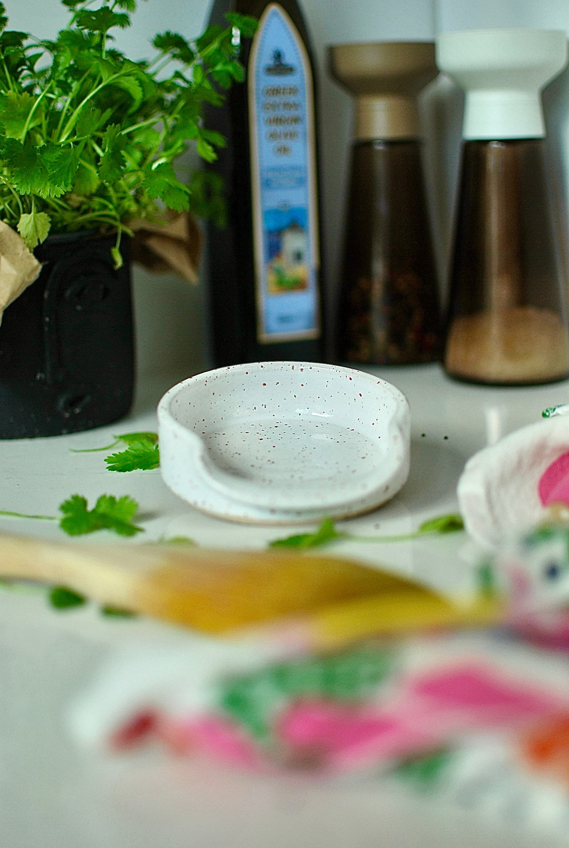 Close-up of handmade ceramic spoon rest, white speckled glaze with scalloped edges, styled with herbs β Chamonix collection, Studio Lippi Ceramics in Ireland