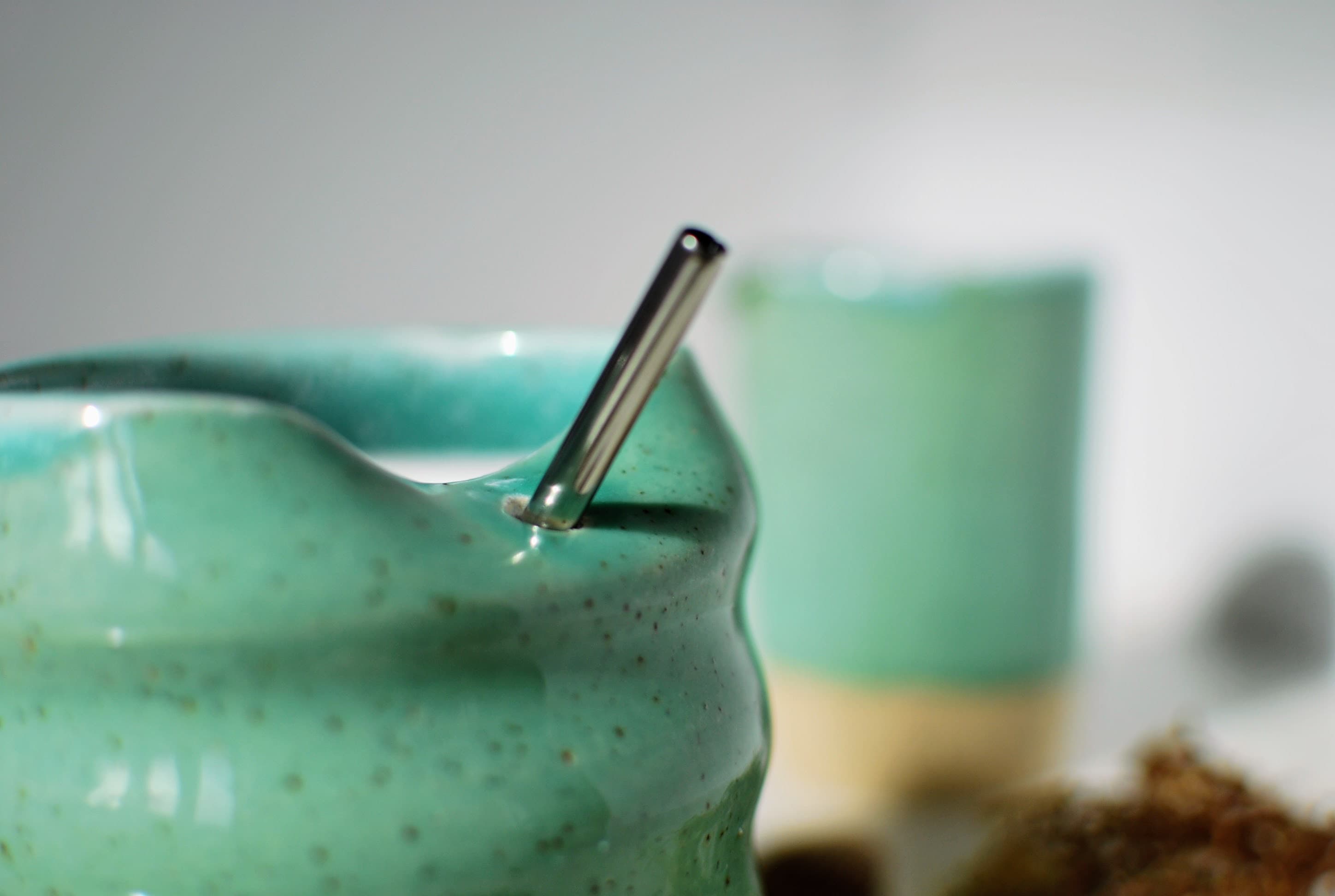 Close-up of a wheel-thrown stoneware tumbler, soft aqua glaze over speckled natural clay base, with stainless steel straw β Maguelone collection, made in Dublin, Ireland