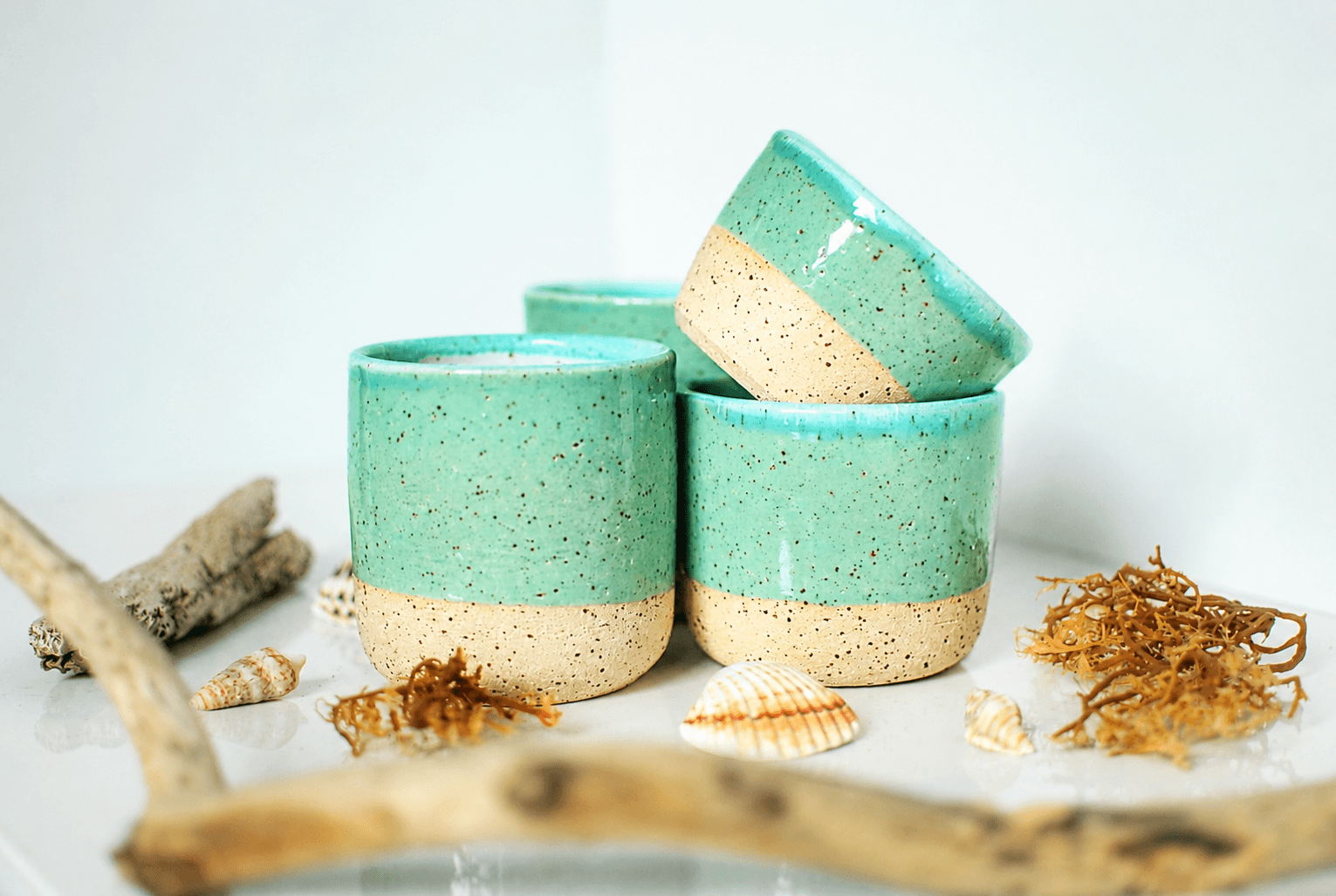 Set of handmade stoneware cups with turquoise glaze and speckled natural clay base, styled with seashells and driftwood β wheel-thrown ceramics made in Dublin, Ireland by Studio Lippi Ceramics